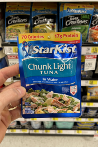 A hand holding a pouch of tuna fish.