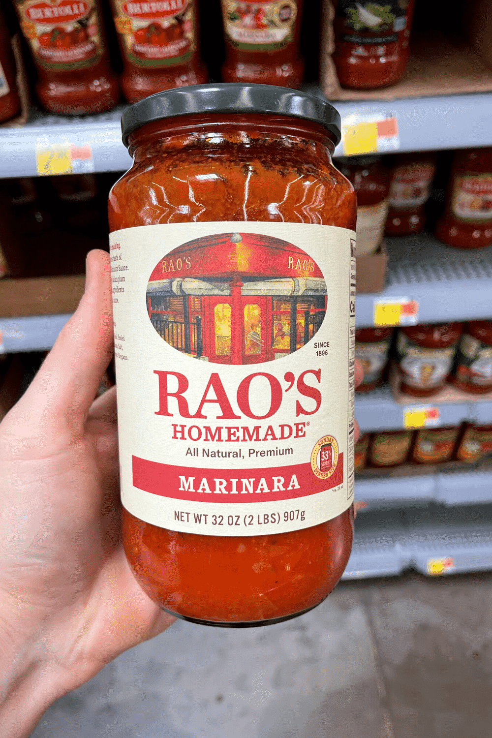 A hand holding a jar of marinara sauce.