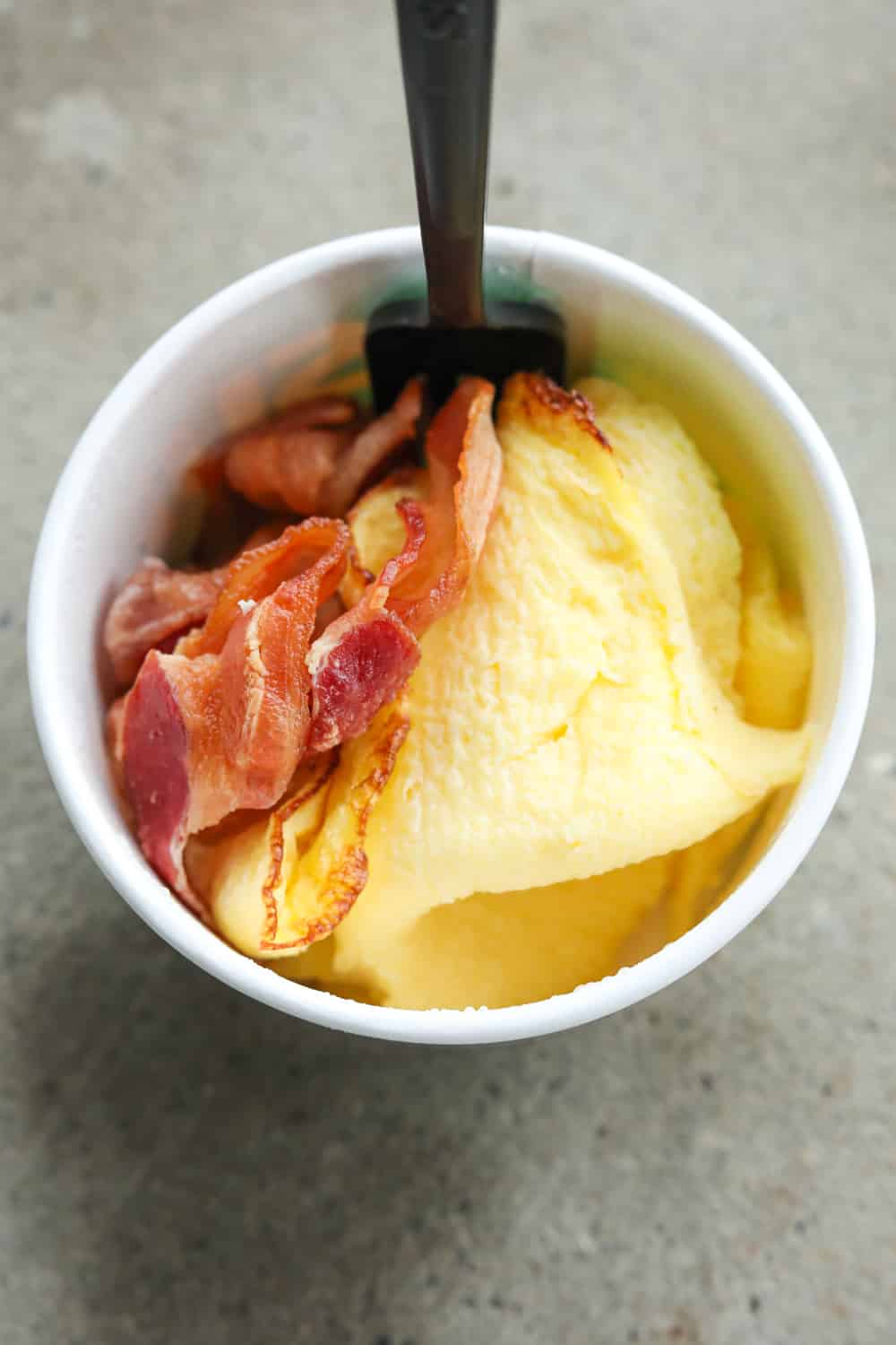 A white cup filled with slices of bacon, scrambled eggs, and cheese.