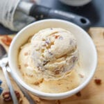 3 Scoops of ice cream in a white bowl that's set on a tan cutting board.