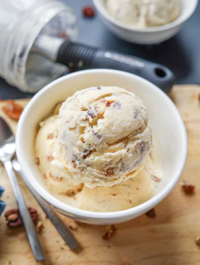 3 Scoops of ice cream in a white bowl that's set on a tan cutting board.