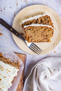 Two slices of carrot bread on a tan plate with a fork next to them.