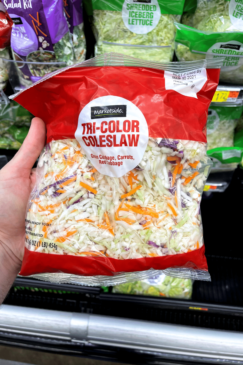 A hand holding a package of coleslaw mix.