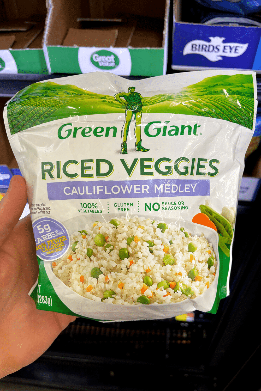 A hand holding a package of frozen riced cauliflower.