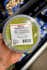 A hand holding a container of guacamole.