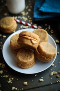 A white plate with 5 peanut butter cookies on it. The plate is set on a baking sheet with a glass of milk, and a blue napkin behind it.