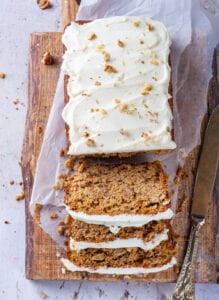 A loaf of carrot cake cutting slices set on top of a cutting board lined with parchment paper.