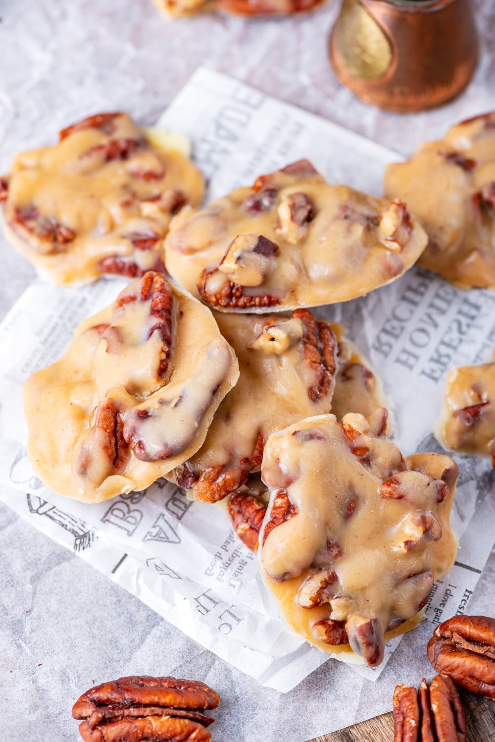 Pralines on a sheet of parchment paper with pecans next to them.