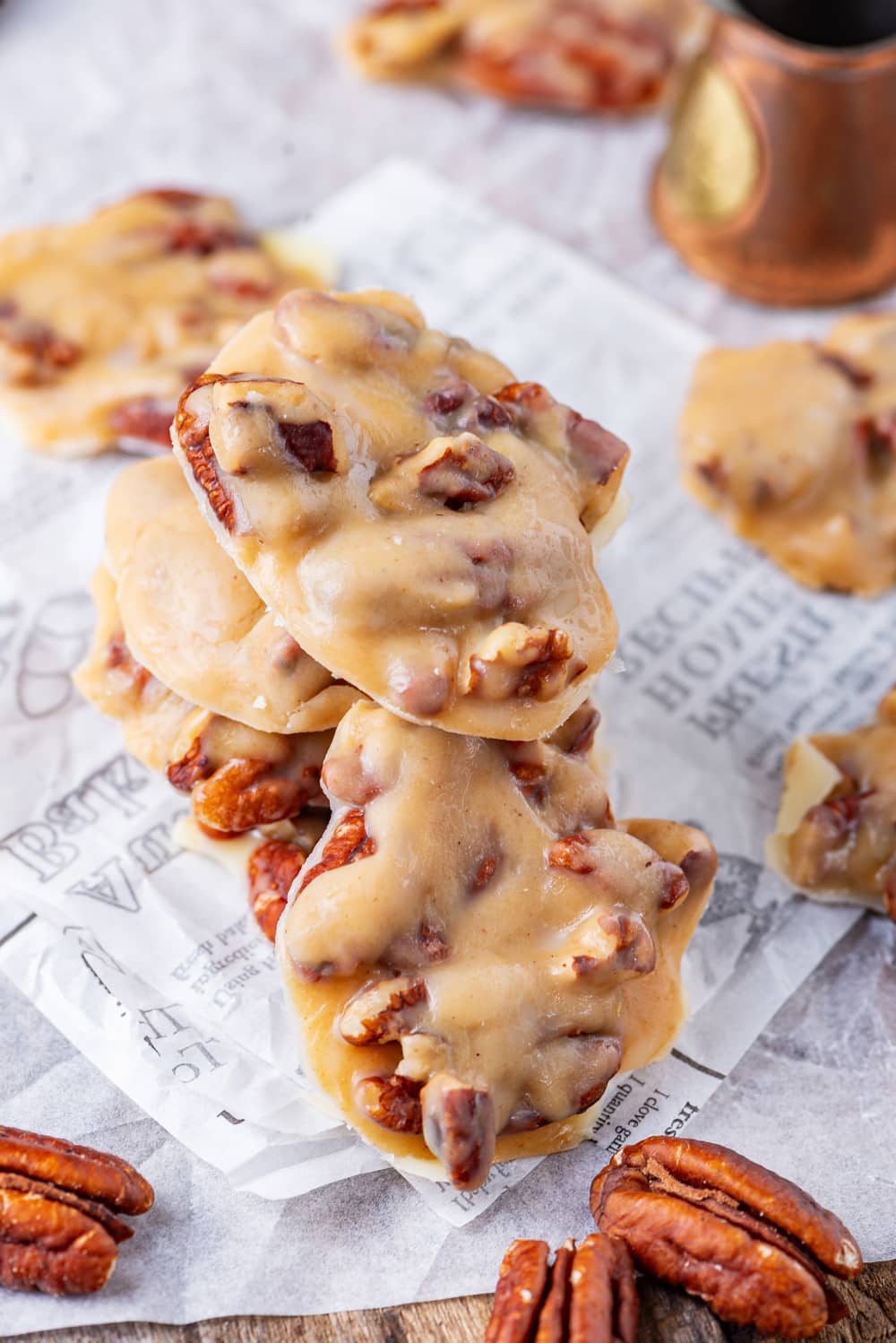 A pile of pralines on parchment paper with pecans placed around them.