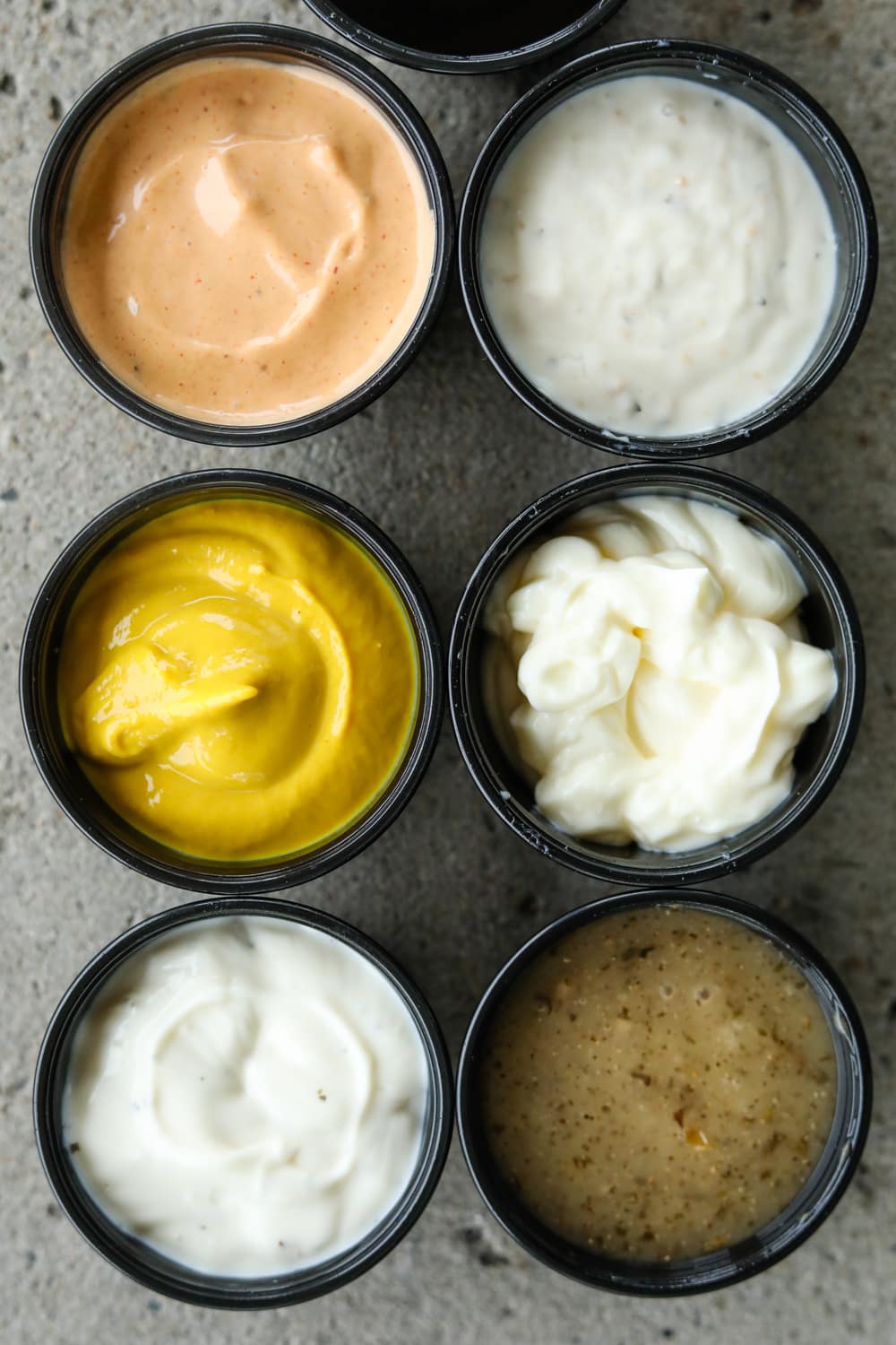 Six black cups filled with different colored sauces.