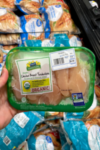 A hand holding a package of organic chicken tenderloins.
