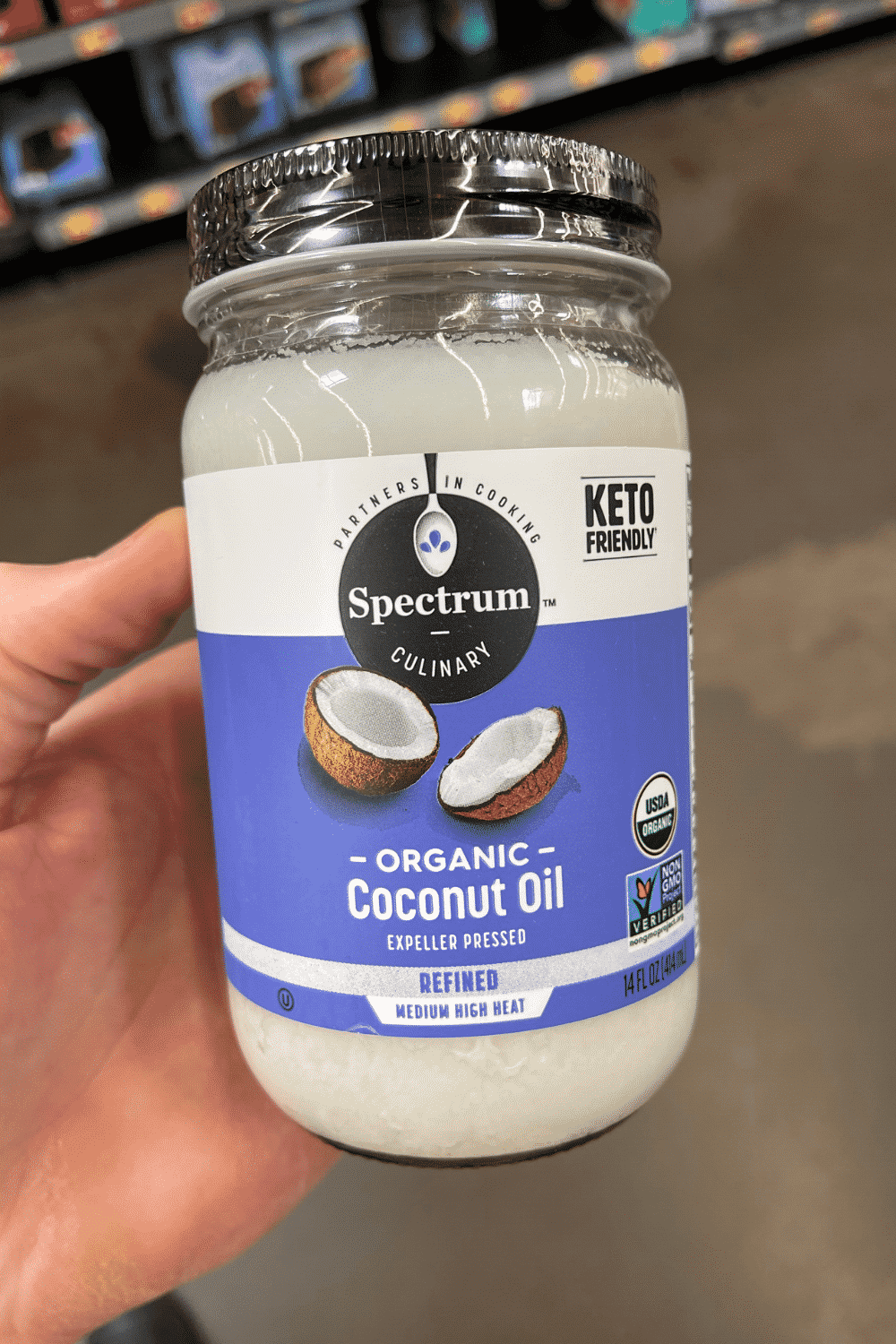 A hand holding a bottle of refined coconut oil.