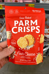 A hand holding a package of Four Cheese Parm crisps