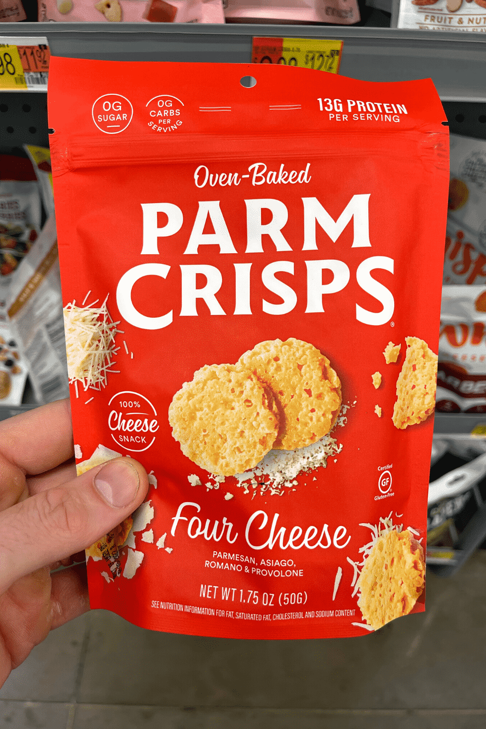 A hand holding a package of Four Cheese Parm crisps