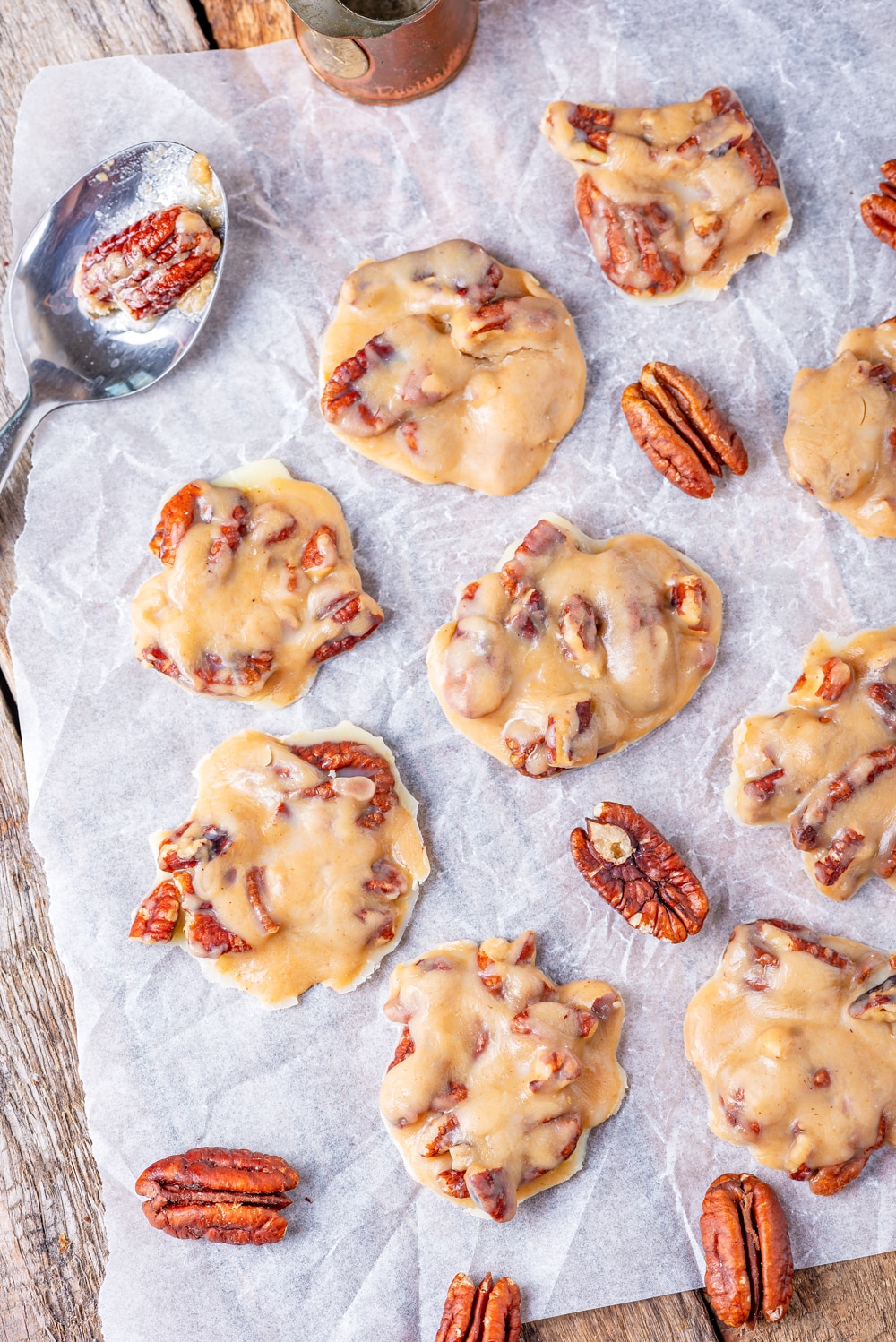 Pralines laid out on a sheet of parchment paper with raw pecans next to them.