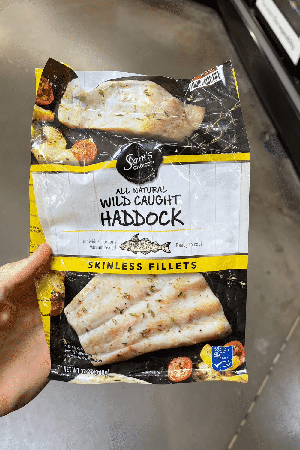 A hand holding a bag of frozen haddock.