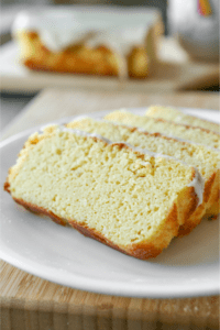 Four slices of poundcake line on one another on a white plate. The whole pound cake is in the background.