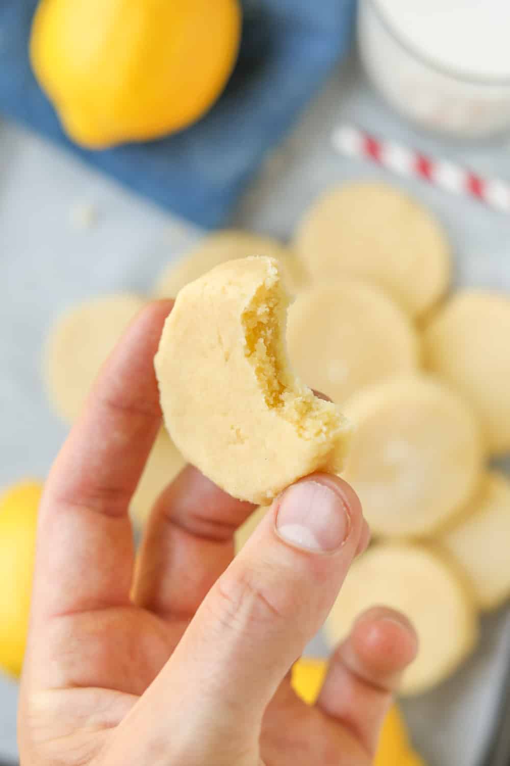 A hand holding a lemon cookie with a bite taken out of it.