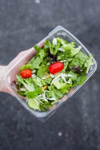 A hand holding a container of side salad from Chick-fil-A.