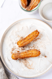 A white play cupboard in a cinnamon sugar mixture. There are two churros on top of the plate