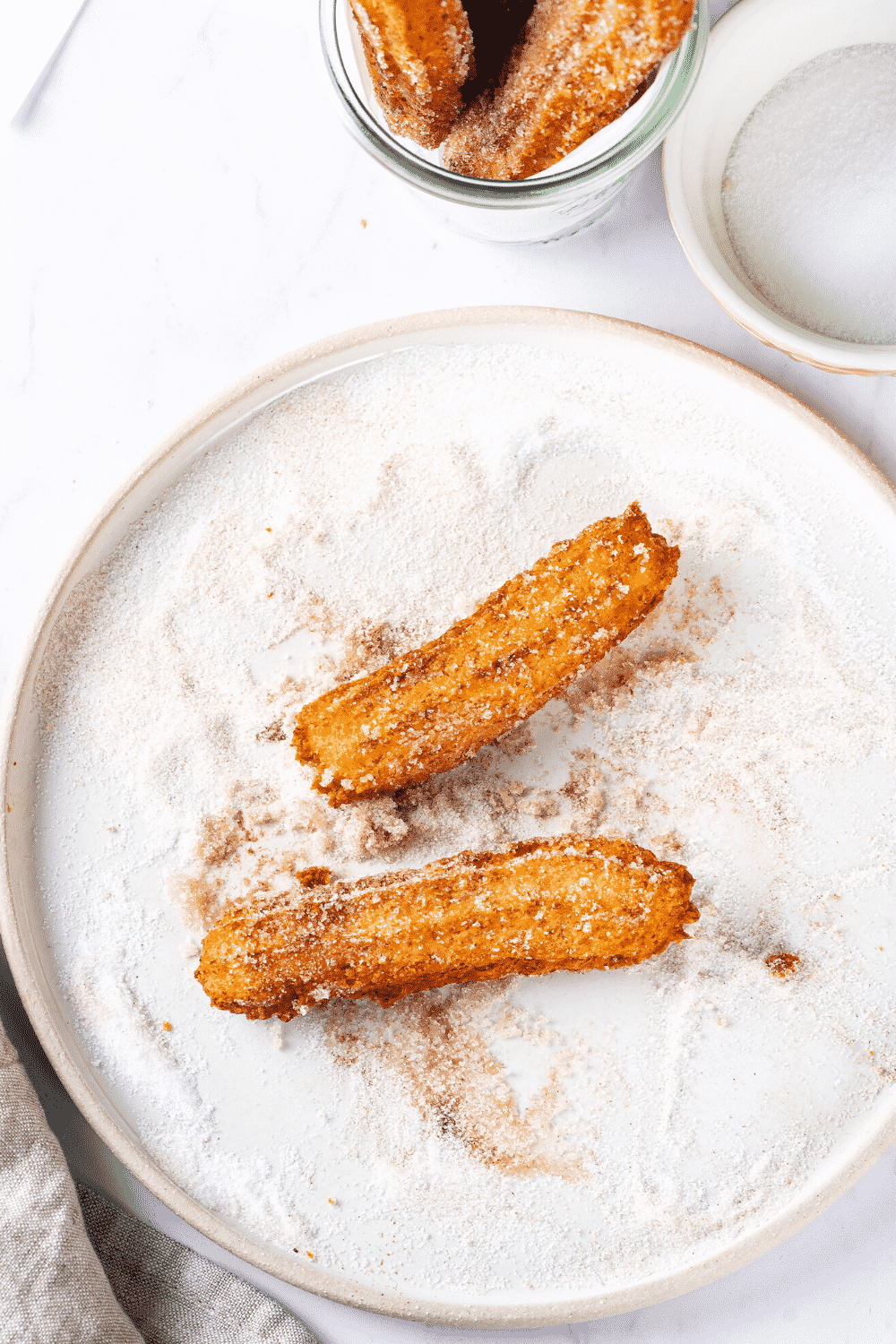 A white play cupboard in a cinnamon sugar mixture. There are two churros on top of the plate