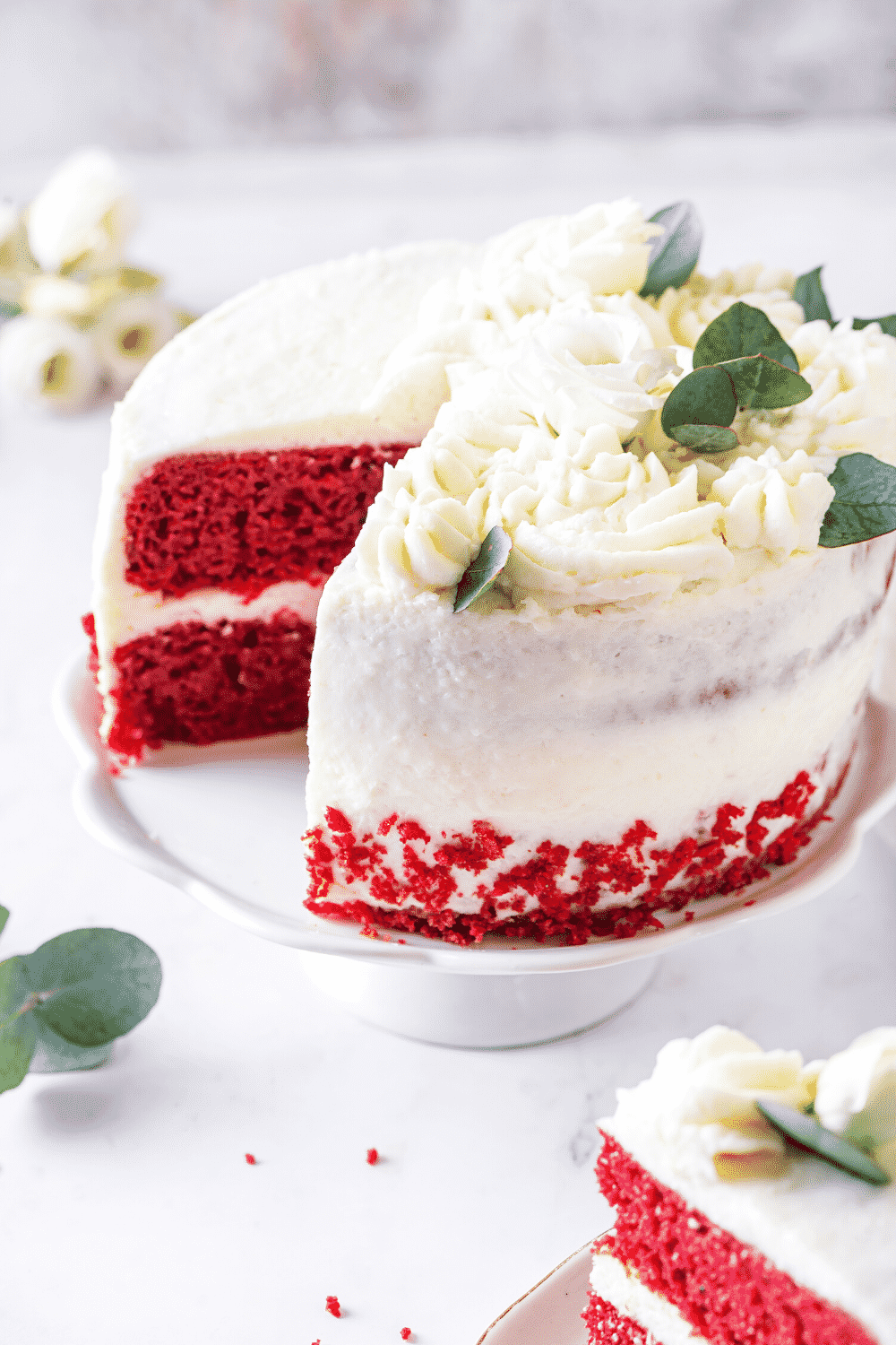 A red velvet cake on a white serving tray with the inside of the cake showing where a piece was taken out.