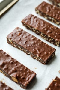 The side of a chocolate candy bar filled with nuts on a baking sheet that's been lined with white parchment paper.