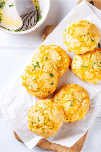 A few keto cheddar biscuits on a piece of white parchment paper on a wooden cutting board.