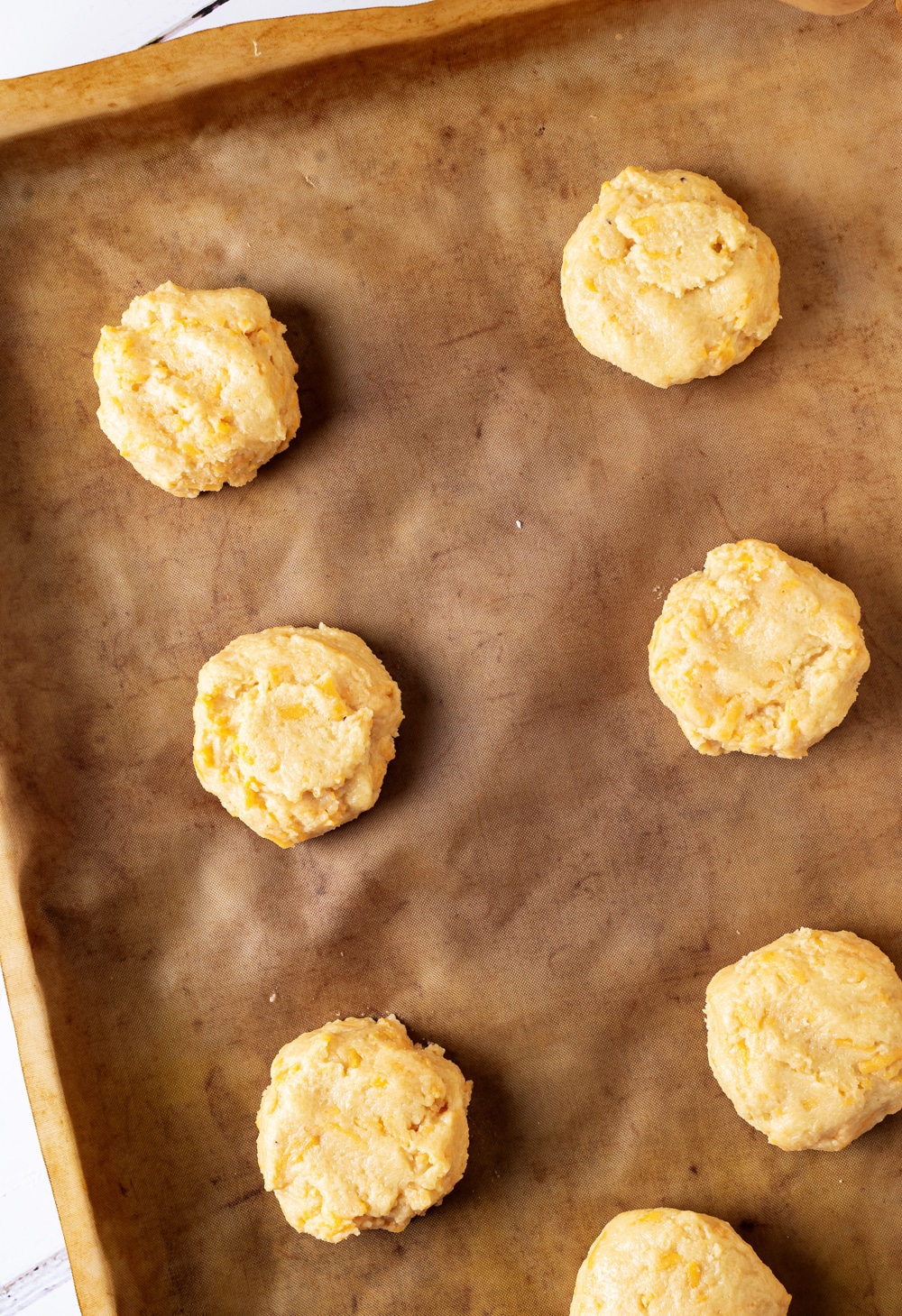 A piece of parchment paper on a baking sheet with seven keto cheddar biscuits on it.