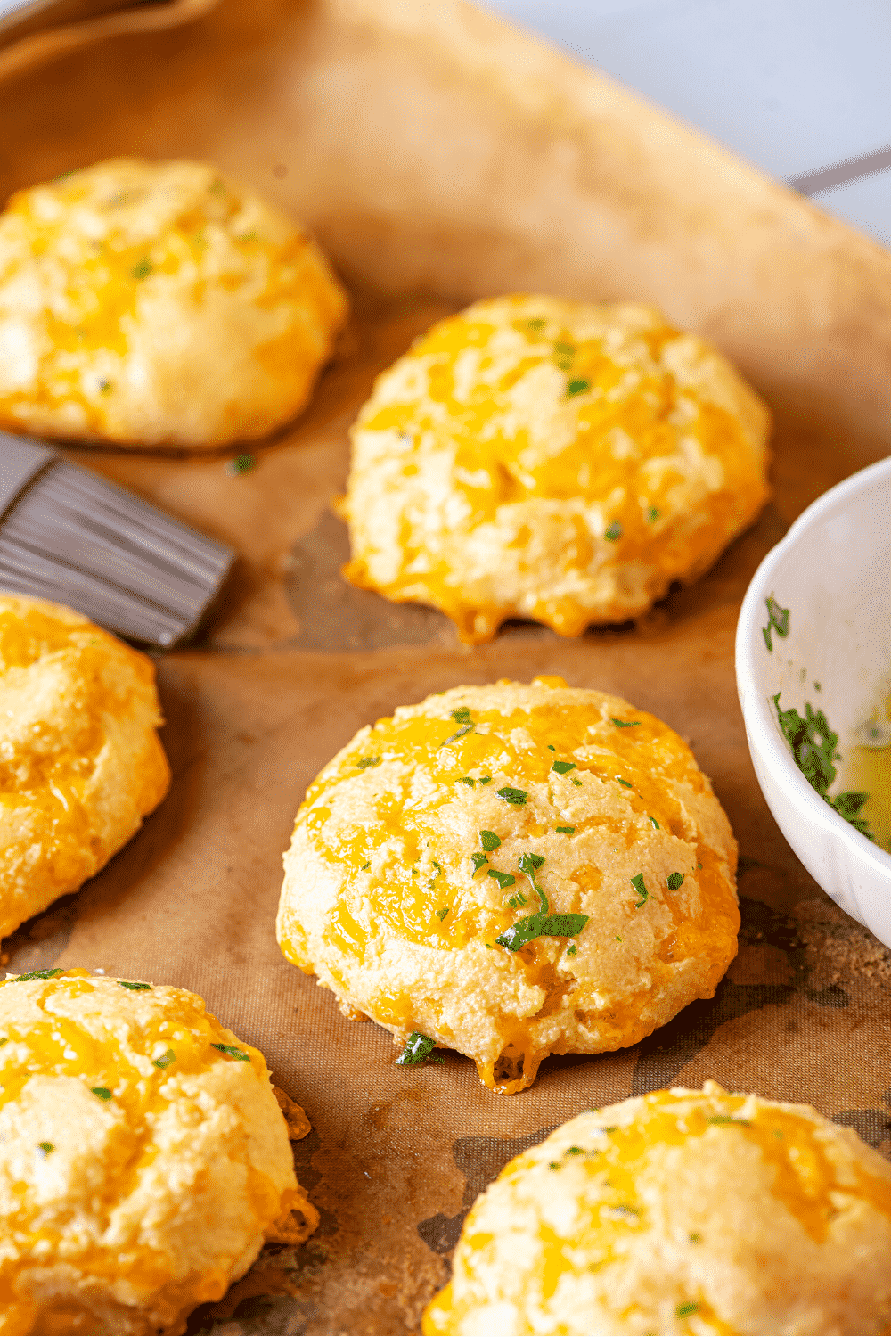 A couple of keto cheddar biscuits on a piece of parchment paper on a baking sheet.