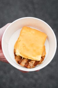 A hand holding a bowl filled with a sausage patty and egg on top and American cheese on the egg.