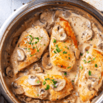 A pan filled with four pieces of chicken marsala. The pan is on a wooden cutting board on a blue counter.