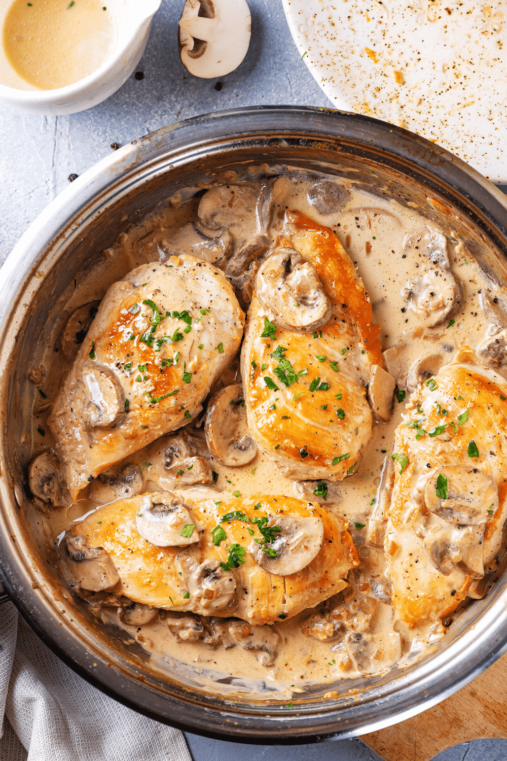 A pan filled with four pieces of chicken marsala. The pan is on a wooden cutting board on a blue counter.