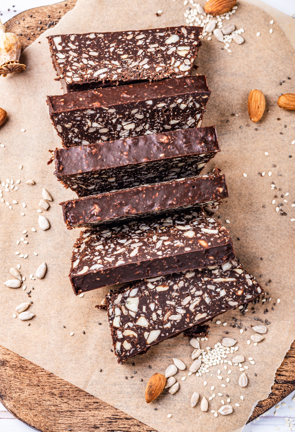 6 Chocolate bars on a brown sheet of parchment paper with various nuts and seeds around them.