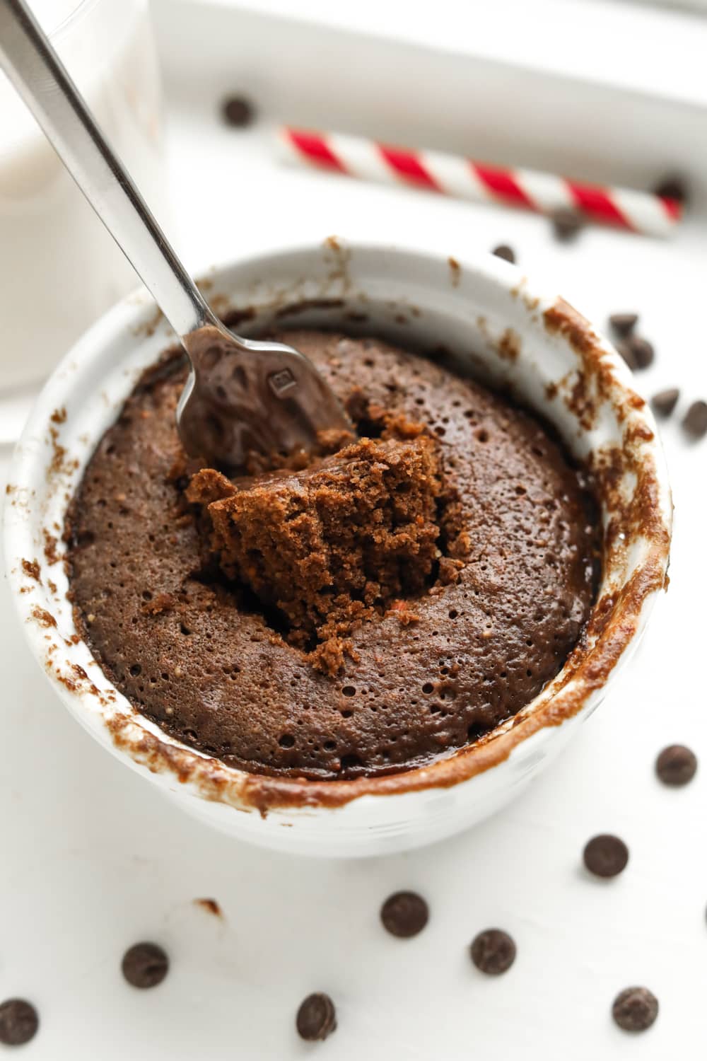 A chocolate cake in a white mug with a fork about to pull a piece of cake out from it.