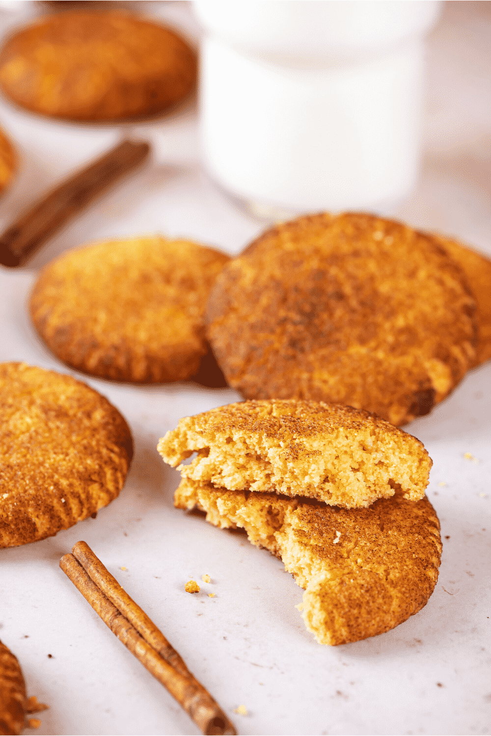 A snickerdoodle cookie that is broken and a half and stacked on itself. There are a few snickerdoodle cookies behind the halved cookie.