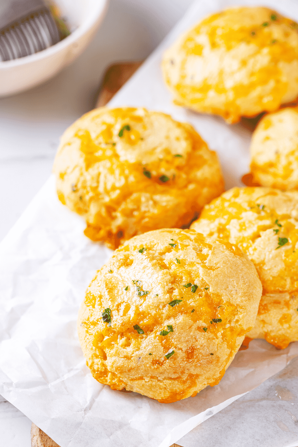 A couple of keto cheddar Bay biscuits on a piece of white parchment paper.