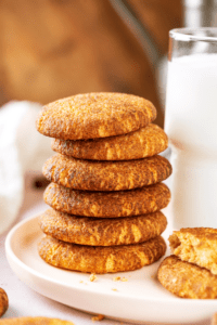 A stack of six snickerdoodle cookies on a white plate. A glass of milk is to the right of the stack.