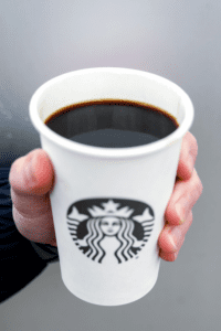 A hand holding a cup of Starbucks dark roast coffee.