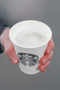 A hand holding a cup of Starbucks espresso macchiato.