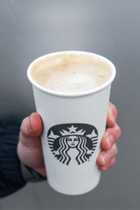 A hand holding a cup of Starbucks blonde vanilla latte.