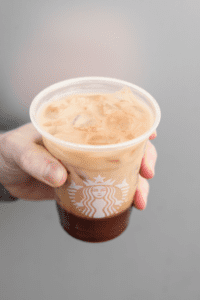 A hand holding a cup of Starbucks chocolate almond milk espresso.