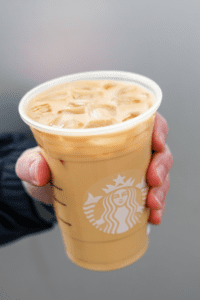 A hand holding a cup of Starbucks iced blonde vanilla latte.