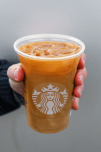 A hand holding a cup of Starbucks iced flat white.