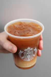 A hand holding a cup of Starbucks iced honey almond milk flat white.