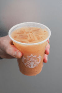 A hand holding a cup of Starbucks iced London fog tea latte.