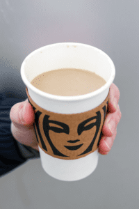 A hand holding a cup of Starbucks latte with almond milk.
