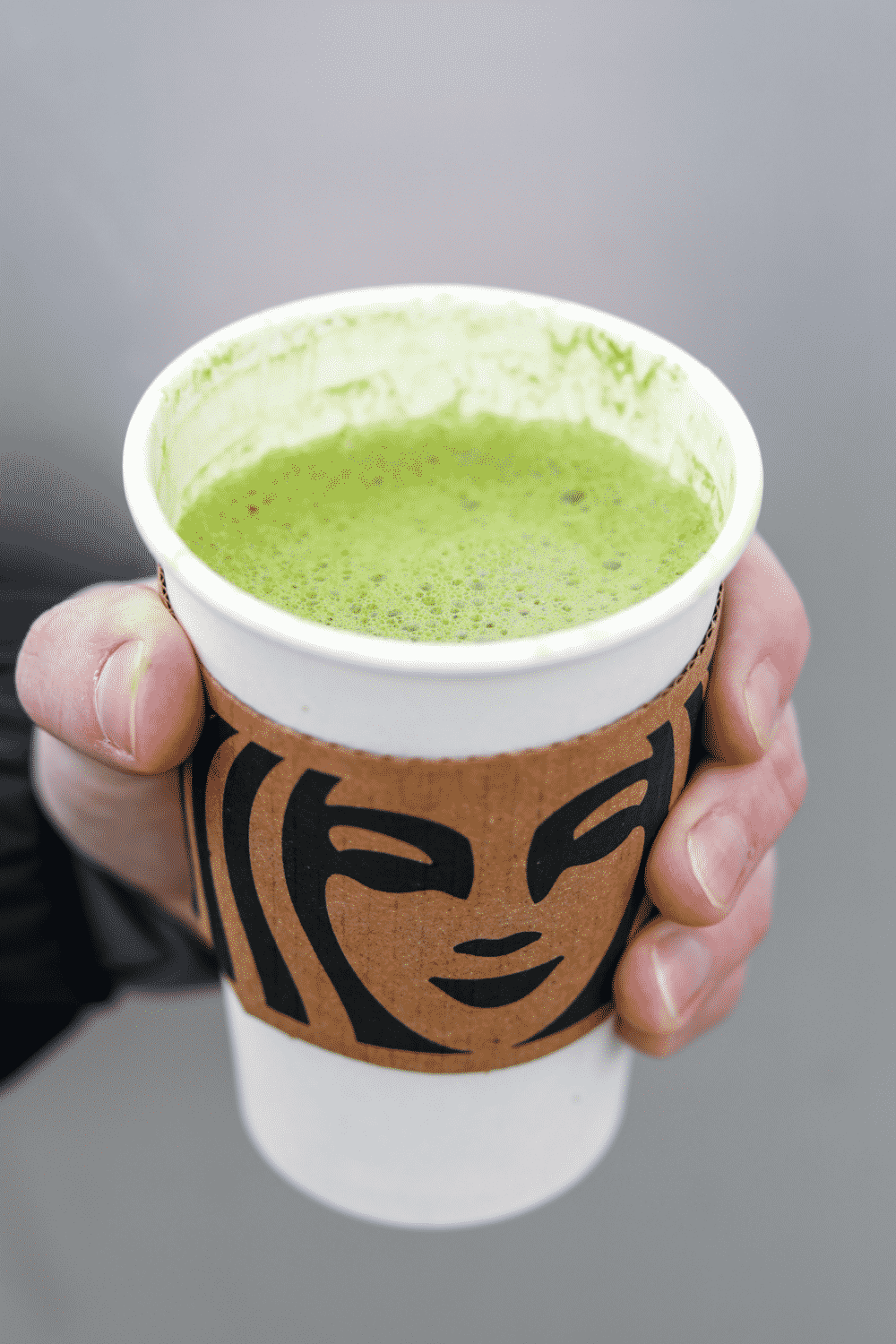 Hand holding a cup of Starbucks matcha latte.