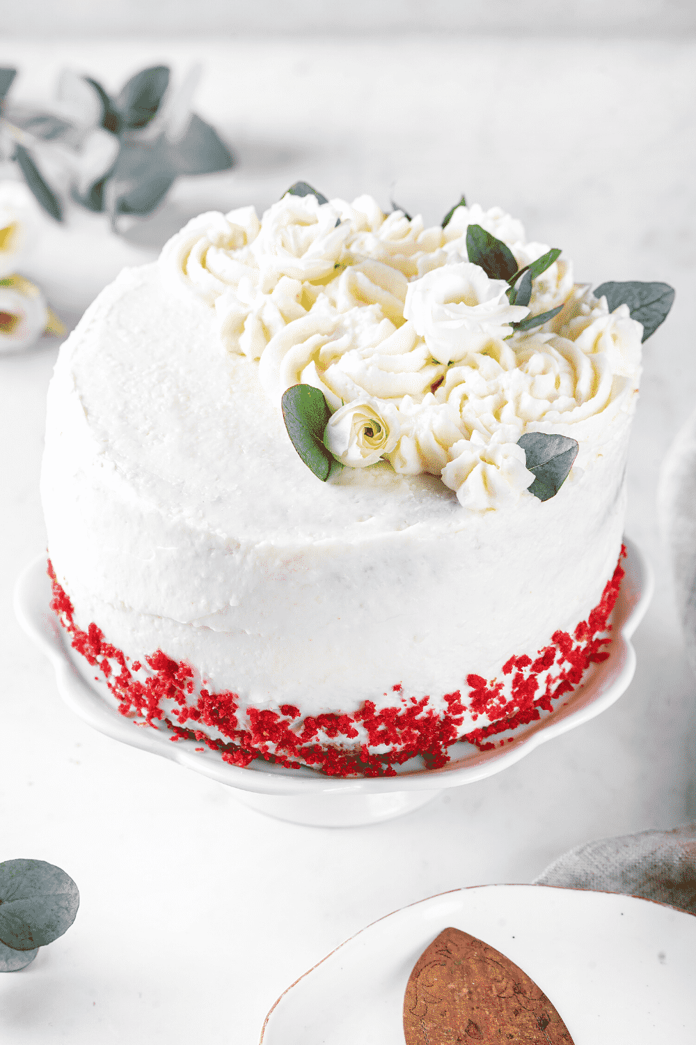 A red velvet cake on a white serving tray that is on a white counter.