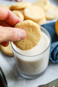 A hand holding a lemon cookie over a glass of milk.